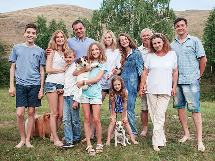Large family portrait outdoors with adults and children wearing white or light blue clothing