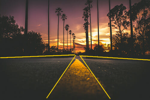 A road way leading to the sunset on a palm tree ladened road