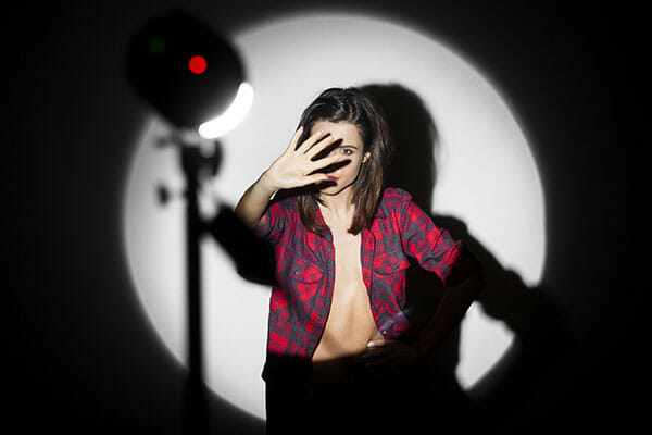 A model in a studio stood in front of a very bright light holding her hand up to shield eyes from the light
