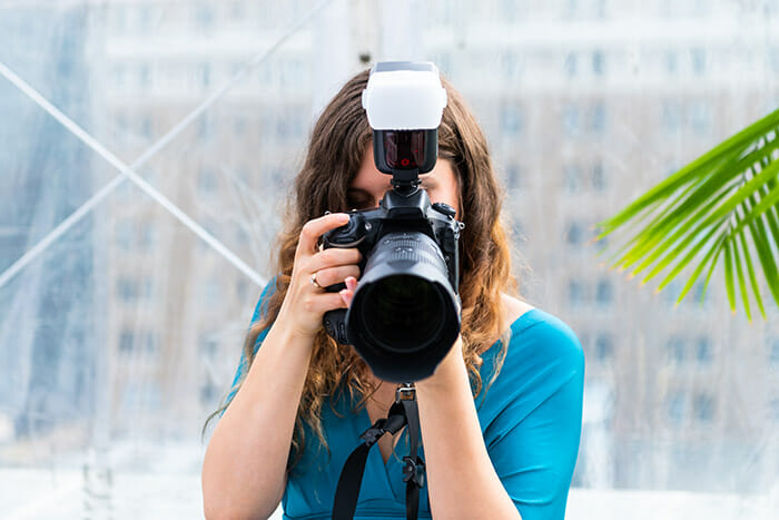A lady taking photos with a camera and a large flash on top with a softbox covering the light