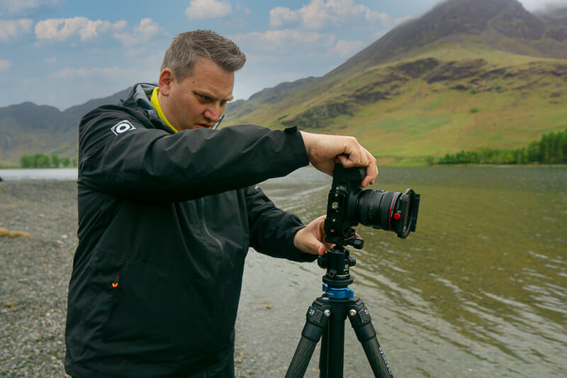 Chris Sale landscape photographer looking at the back of a camera at the side of buttermere lake in the lake district