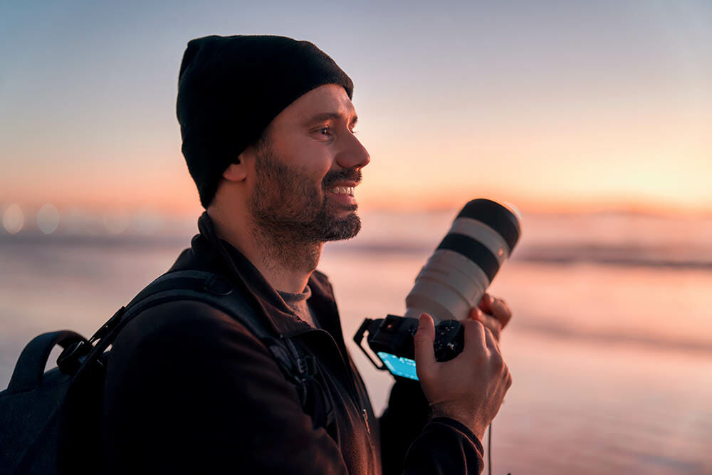 latin mature photographer holding professional camera on the beach and smiling happy portrait