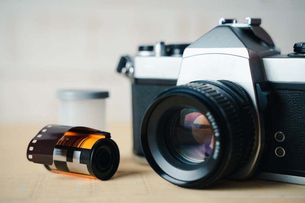 Old SLR film camera and a roll of film on wooden background.