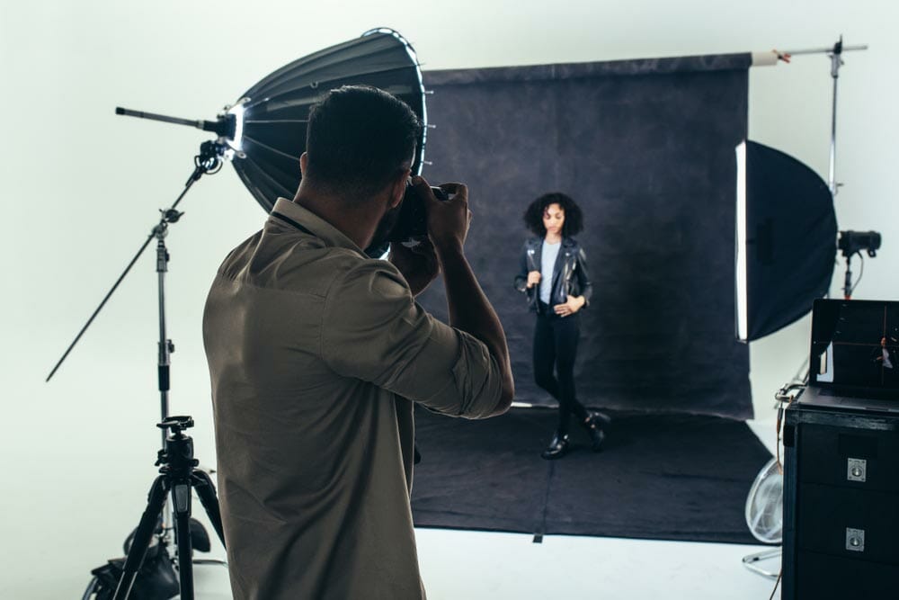 Model posing for a photograph during a photo shoot. Studio shot of a photographer shooting photos of a woman with studio flash lights on.